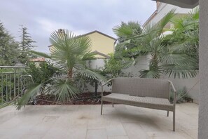 A patio with a wicker bench, surrounded by potted plants and a metal railing. - Apartments Delfin Villa Sofia (Umag)