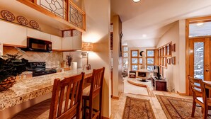 A kitchen with a granite countertop, wooden chairs, a microwave, and a stove.