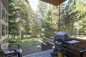 A deck with a grill, a chair, and a view of a forest. - River Glen Condos by CRMR (Frisco)