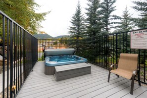 Una terrazza con idromassaggio e una sedia, circondata da una recinzione metallica e alberi.