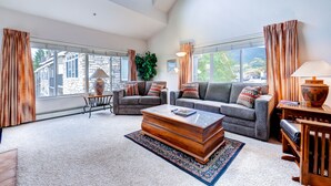 A spacious living room with a large window, two sofas, a coffee table, and a rug. - Bay Club Town Homes by CRMR (Frisco)