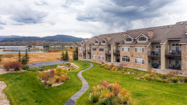 A multi-story building with a stone facade, multiple balconies, and a landscaped lawn with a winding path. - Bay Club Town Homes by CRMR (Frisco)