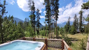 Un jacuzzi en una terraza de madera con vistas a un bosque y montañas.