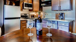 A modern kitchen with wooden cabinets, stainless steel appliances, and a wine bottle on the counter. - Cedars Lodge Condos by CRMR (Frisco)