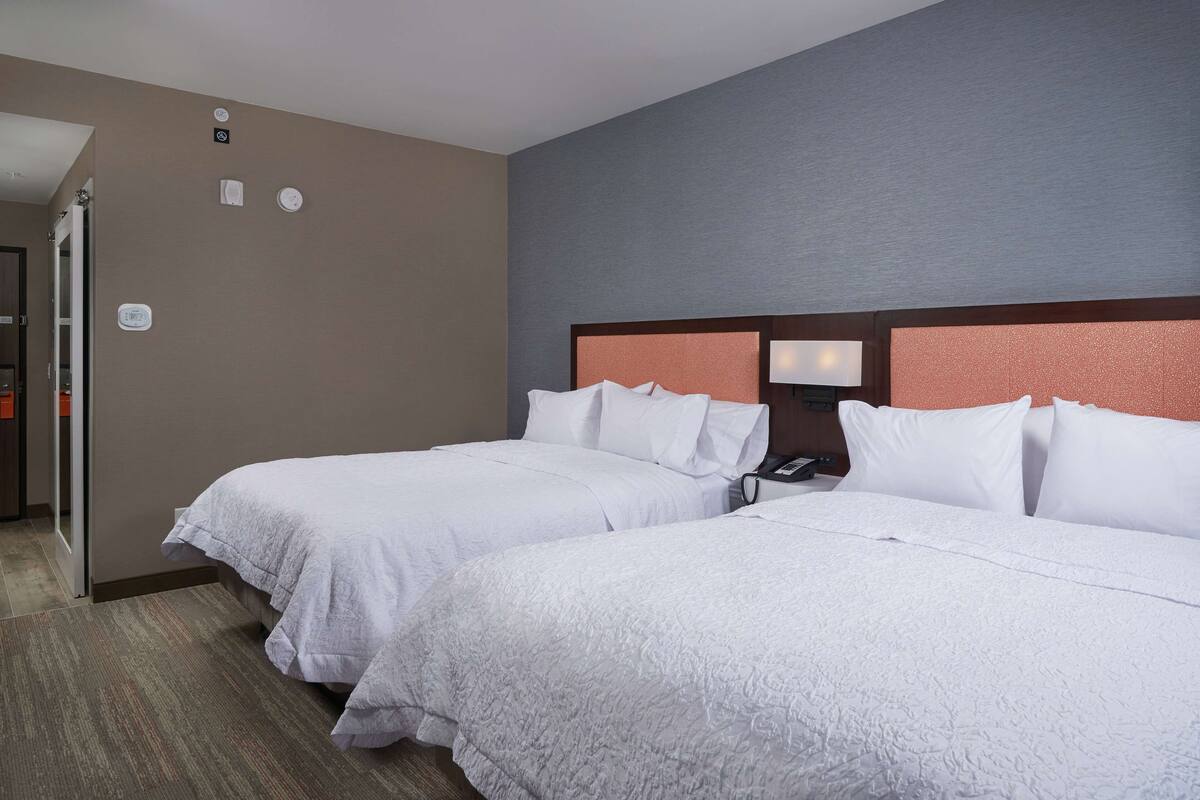A hotel room with two beds, a wooden headboard, a nightstand, and a wall-mounted phone.