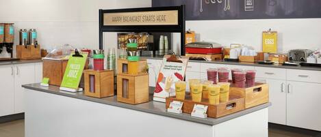 A breakfast bar with a sign indicating 'Happy Breakfast Starts Here' and various food items and drinks displayed.