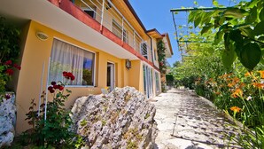 A yellow building with a balcony, a stone pathway, and surrounding greenery.