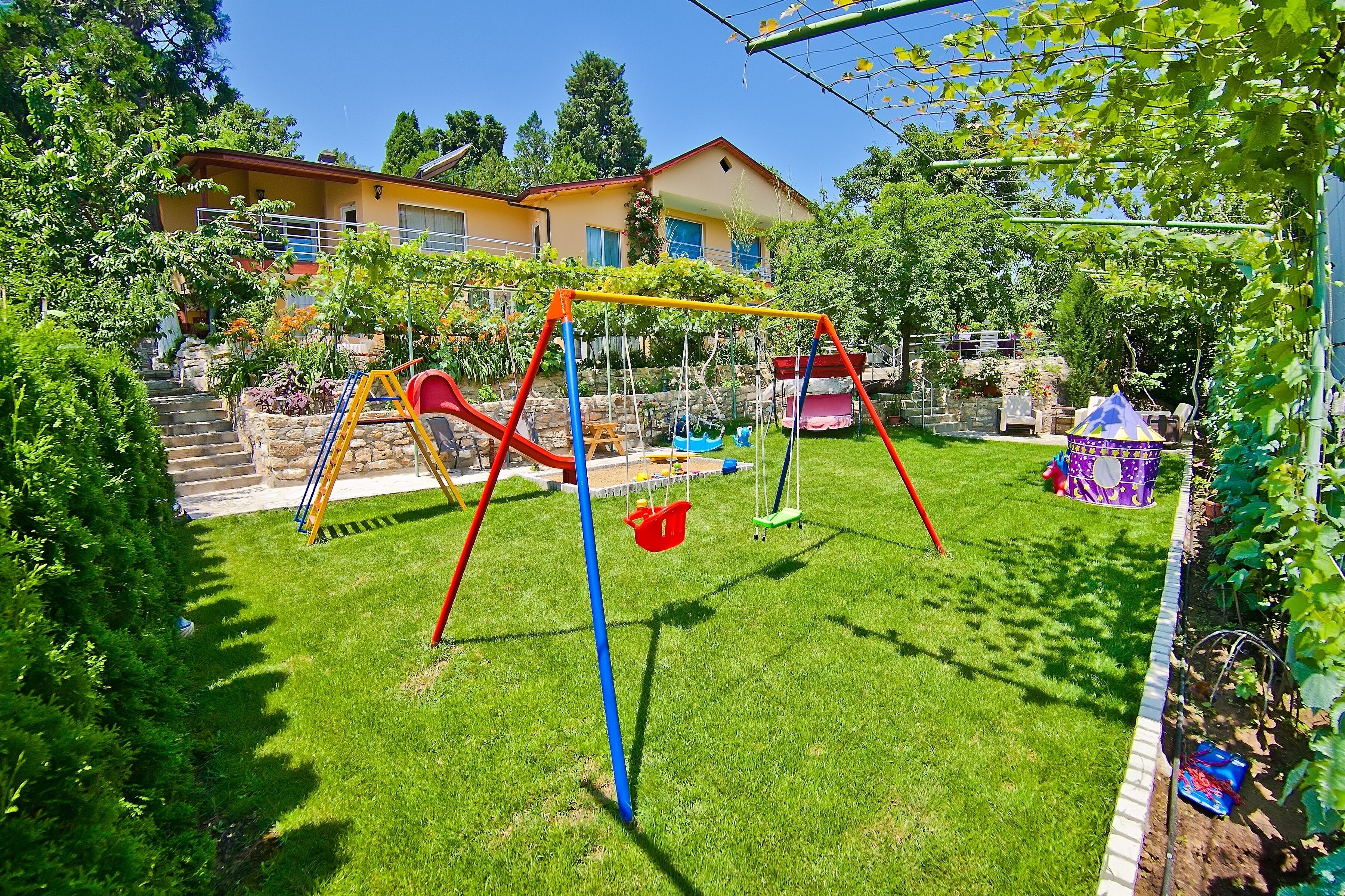 A well-maintained garden with a swing set, a small playhouse, and a stone staircase leading to a house.