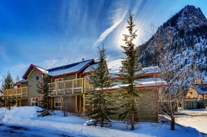 A two-story lodge with a balcony, surrounded by snow-covered trees and mountains.
