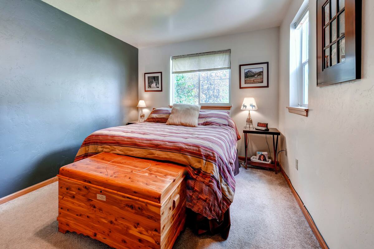A bedroom with a bed, a nightstand, a window, and a suitcase.