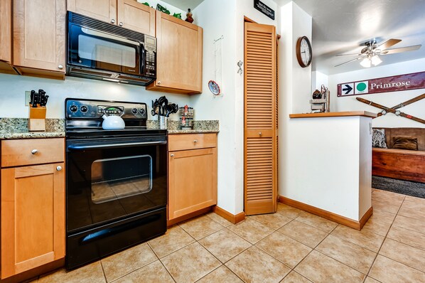 A kitchen with wooden cabinets, a black oven, a microwave, and a clock on the wall.