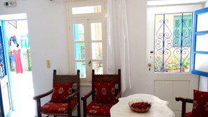 A room with two wooden chairs with red cushions, a white table with a bowl of fruit, and a window with decorative iron bars. - Entire Family Friendly House "Villa Archondisa" in the Old Town (Χανιά)