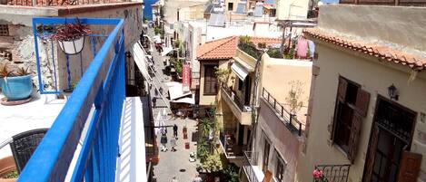 Un carrer estret amb edificis a ambdós costats, balcons amb plantes i una vista clara del mar al fons.