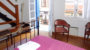 A bedroom with a wooden staircase, a bed with a pink bedspread, two chairs, a window, and an open door leading to a balcony. - Entire Family Friendly House "Villa Archondisa" in the Old Town (Χανιά)