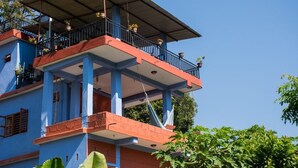 Un edificio de varios pisos con un balcón en el nivel superior, sostenido por columnas azules y un zócalo rojo.