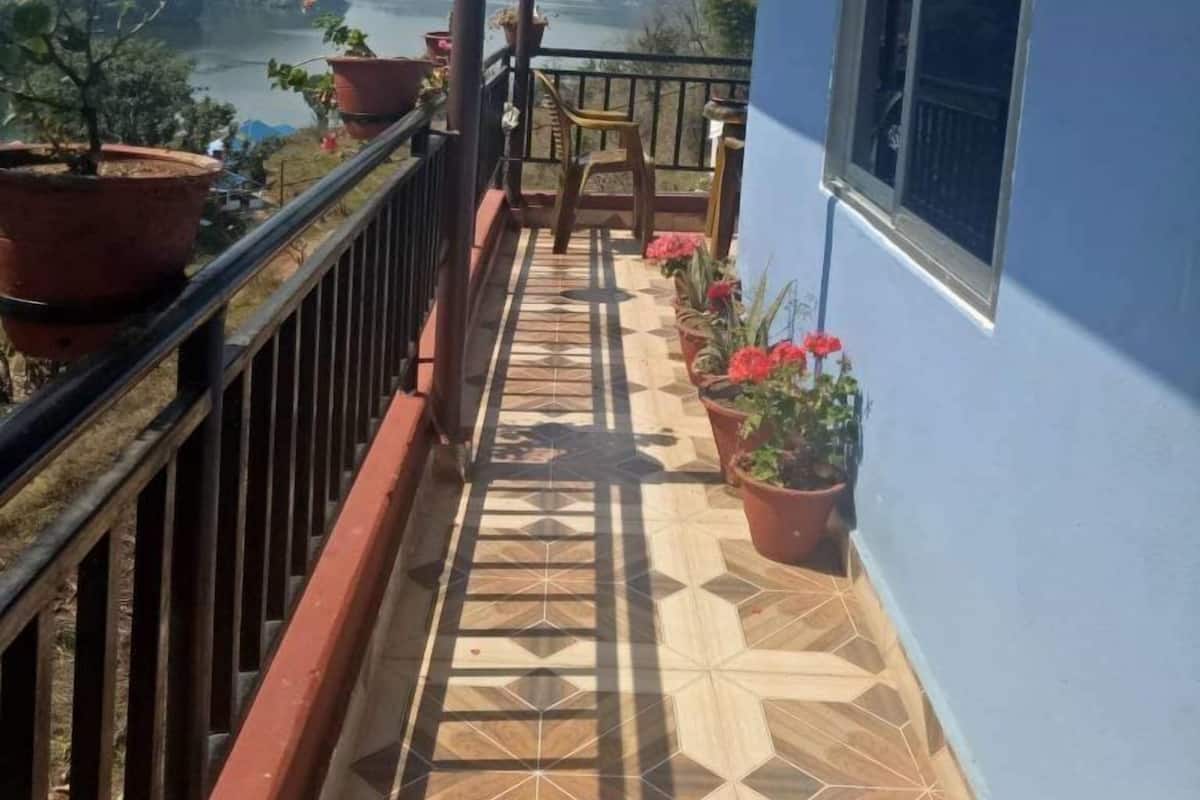 Un balcón con vista a un lago y montañas, plantas en macetas y suelo de baldosas.