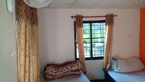 Una habitación con cama, ventana con cortinas, ventilador de pie y aire acondicionado de pared.