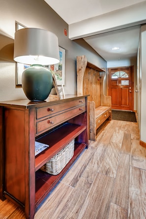 A hallway with a wooden bench, a lamp, and a door. - The Pointe Town Homes by CRMR (Frisco)