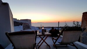 Une terrasse avec deux chaises et une table, d’où l’on peut admirer le coucher de soleil sur la mer.
