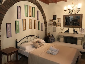 A bedroom with a bed, a nightstand, a fireplace, and framed pictures on the wall.