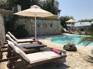 A poolside area with lounge chairs and umbrellas, a stone wall, and a clear blue pool.