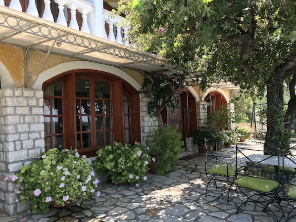 A stone-paved courtyard with a wooden door, potted plants, and outdoor furniture.