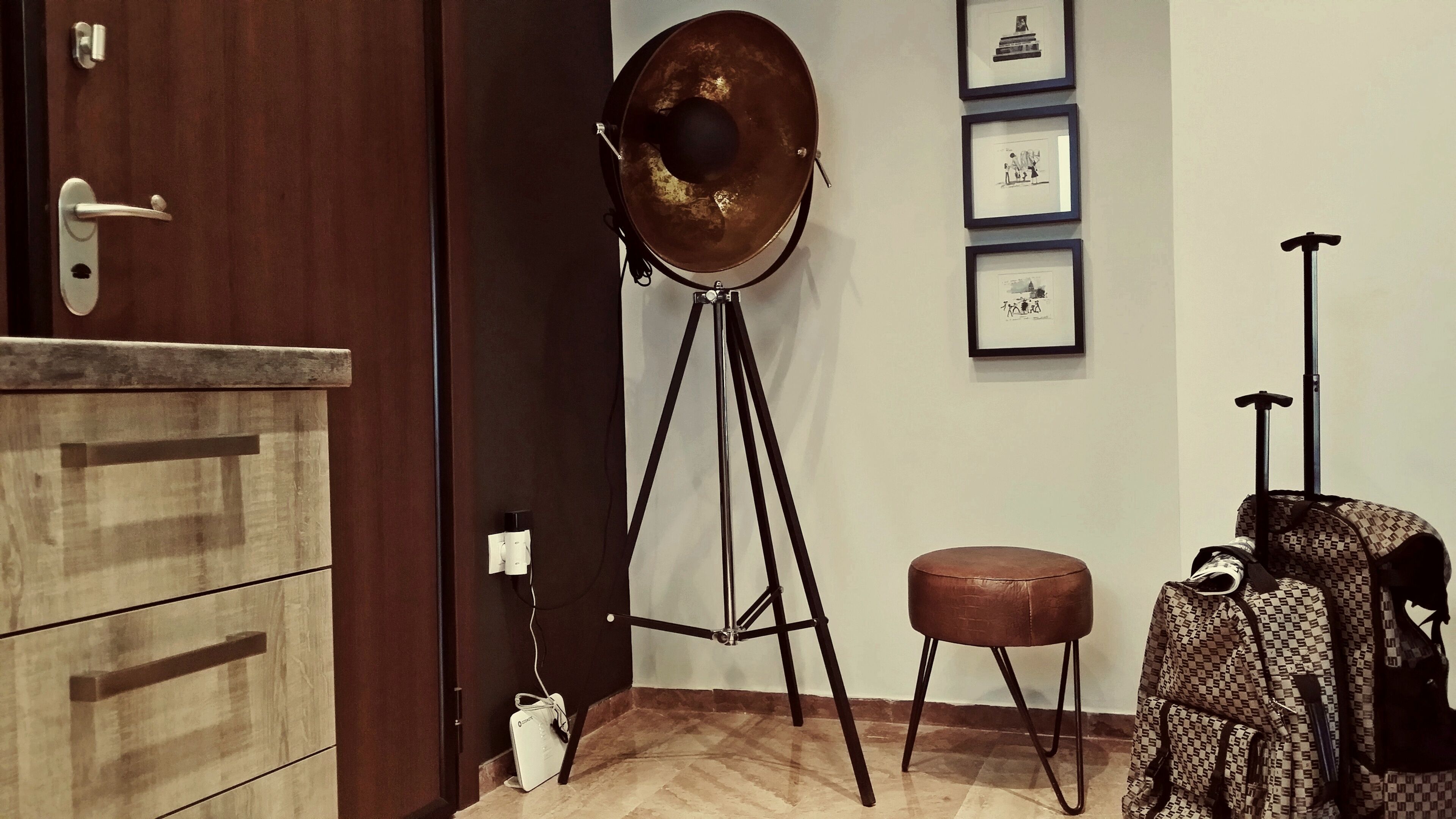 A room with a wooden cabinet, a tripod lamp, a framed picture on the wall, and a patterned bag.