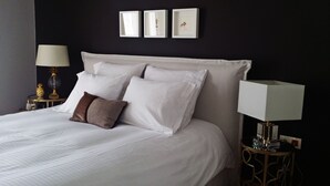 A neatly made bed with white linens and two pillows, a bedside lamp, and three framed pictures on the wall above the bed. - Atenéo, a modern flat downtown Athens! AMA 00000054917 (Αθήνα)