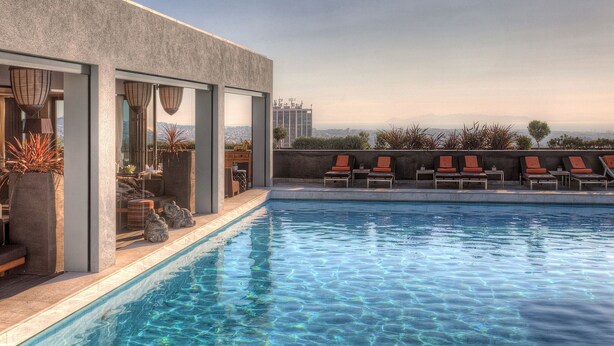 A rooftop pool with clear blue water, surrounded by lounge chairs and potted plants, overlooking a cityscape. - Atenéo, a modern flat downtown Athens! AMA 00000054917 (Αθήνα)