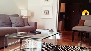 A modern living room with a glass coffee table, a sofa, a chair, and framed artwork on the wall. - Atenéo, a modern flat downtown Athens! AMA 00000054917 (Αθήνα)