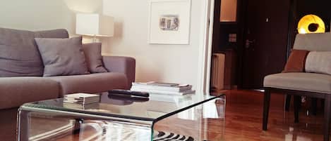 A modern living room with a glass coffee table, a sofa, a chair, and framed artwork on the wall.