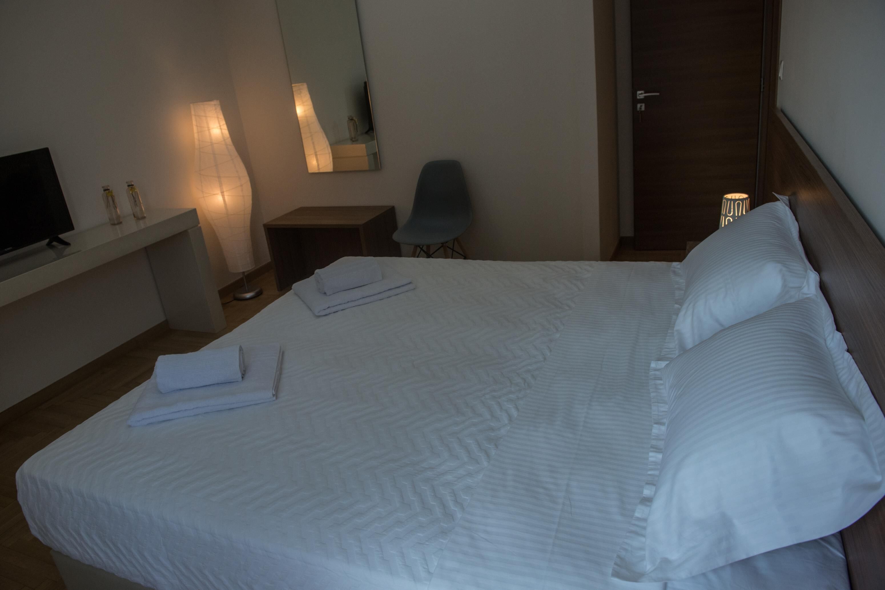 Ein Hotelzimmer mit einem aufgeräumten Bett, einem Fernseher auf einem Tisch, einem Sessel und einem Schreibtisch mit Lampe.