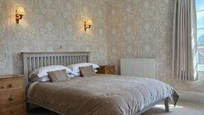 A bedroom with a bed, two bedside tables, a nightstand, a radiator, and two wall-mounted lamps.