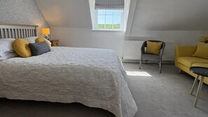 A bedroom with a large bed, a chair, a sofa, a window, and a radiator. - Lower Bryanston Farm (Blandford Forum)