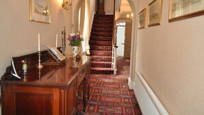 A hallway with a wooden desk, framed pictures, and a patterned carpet leading to a staircase.
