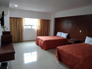 Habitación de hotel con dos camas, un armario de madera, un escritorio con silla y una ventana con cortinas.