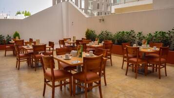 A rooftop dining area with multiple tables and chairs, surrounded by potted plants.