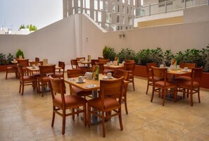 Zona de comedor en la azotea con varias mesas y sillas, rodeada de plantas en macetas.