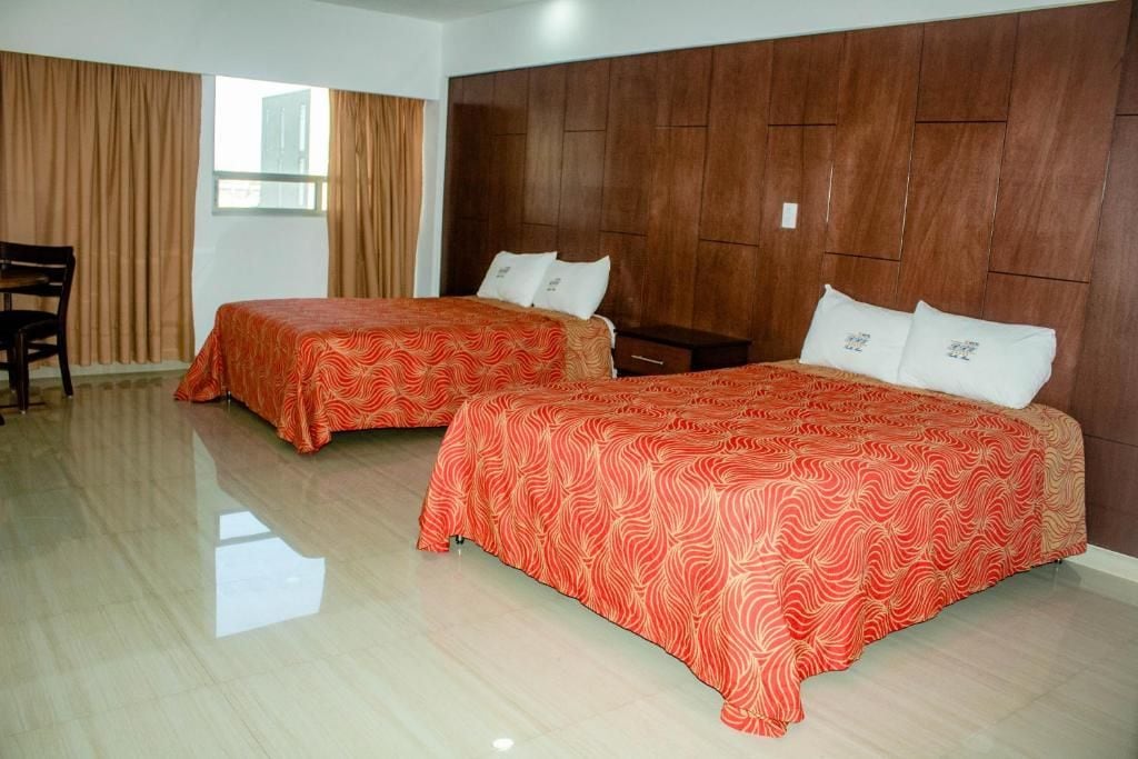 A hotel room with two beds, a wooden headboard, a small table, and a chair.