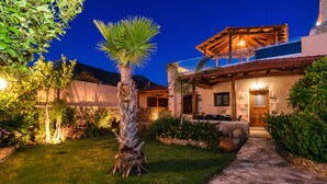 A well-lit residential property with a stone pathway leading to a wooden door, surrounded by lush greenery and flowering plants. - Luxury stone villa with outdoor jacuzzi, private pool and antique furniture (Πλάκα)