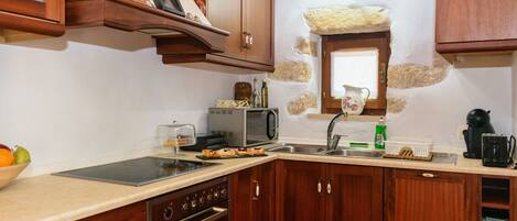 Una cocina con armarios de madera, microondas, lavamanos y cafetera.