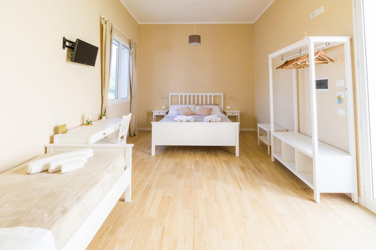 Quarto com cama, mesas de cabeceira, guarda-roupa e televisão fixada na parede.