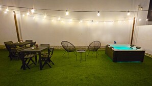 En udendørs terrasse med spisebord, stole, jacuzzi og lyskæder.