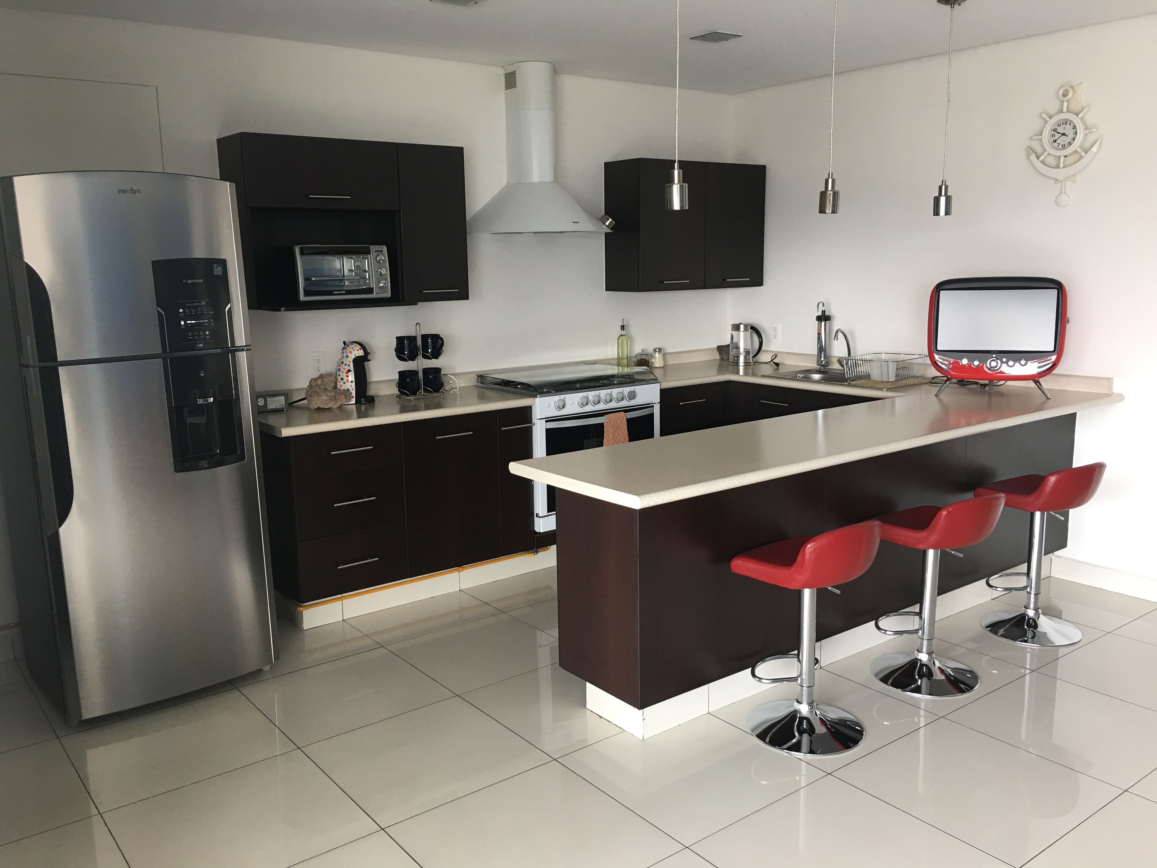 Uma cozinha moderna com eletrodomésticos de aço inoxidável, uma ilha central com banquetas e um micro-ondas sobre o forno.