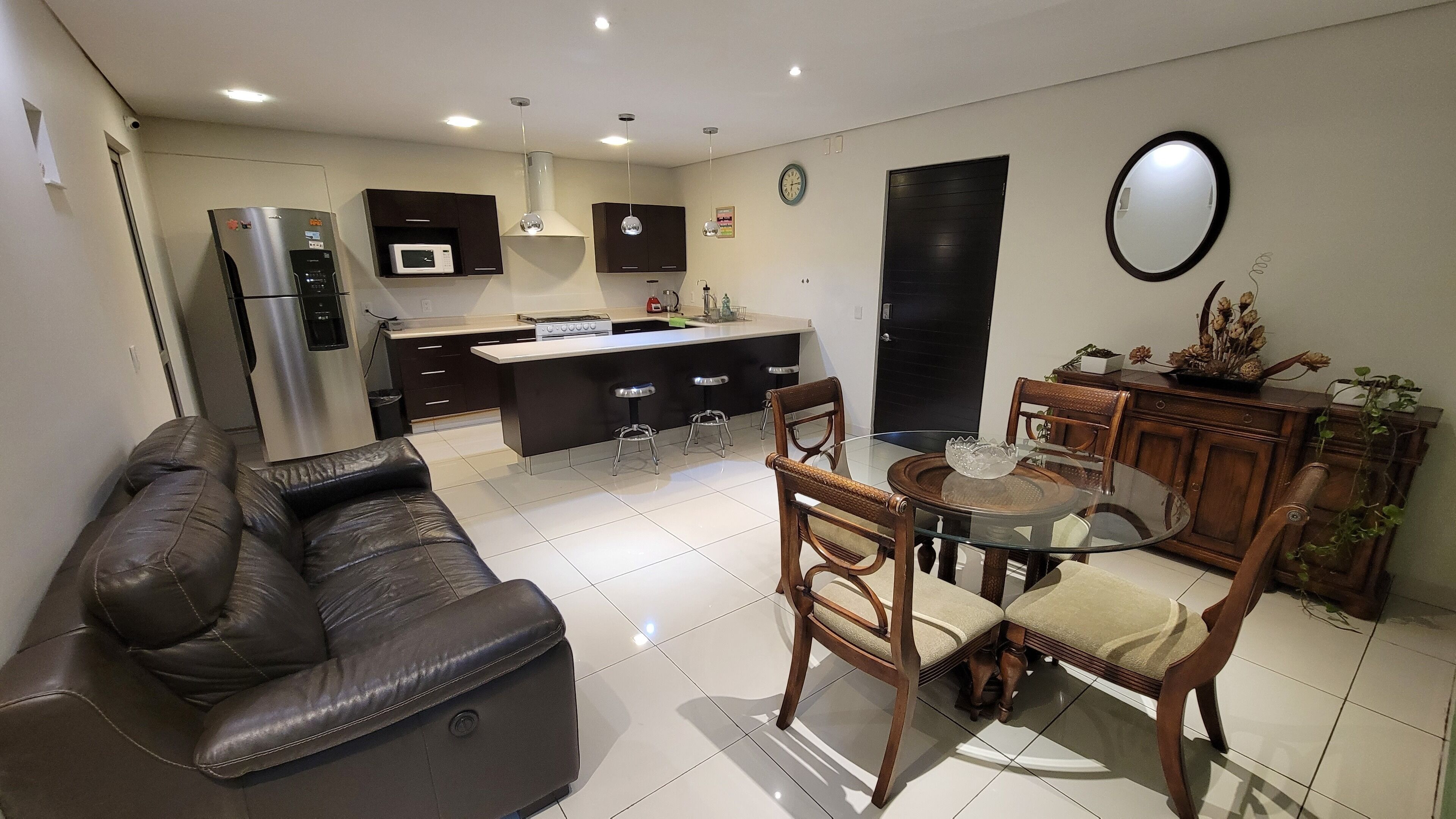 A modern kitchen with a central island, a dining area with a glass table, and a living room with a leather sofa.