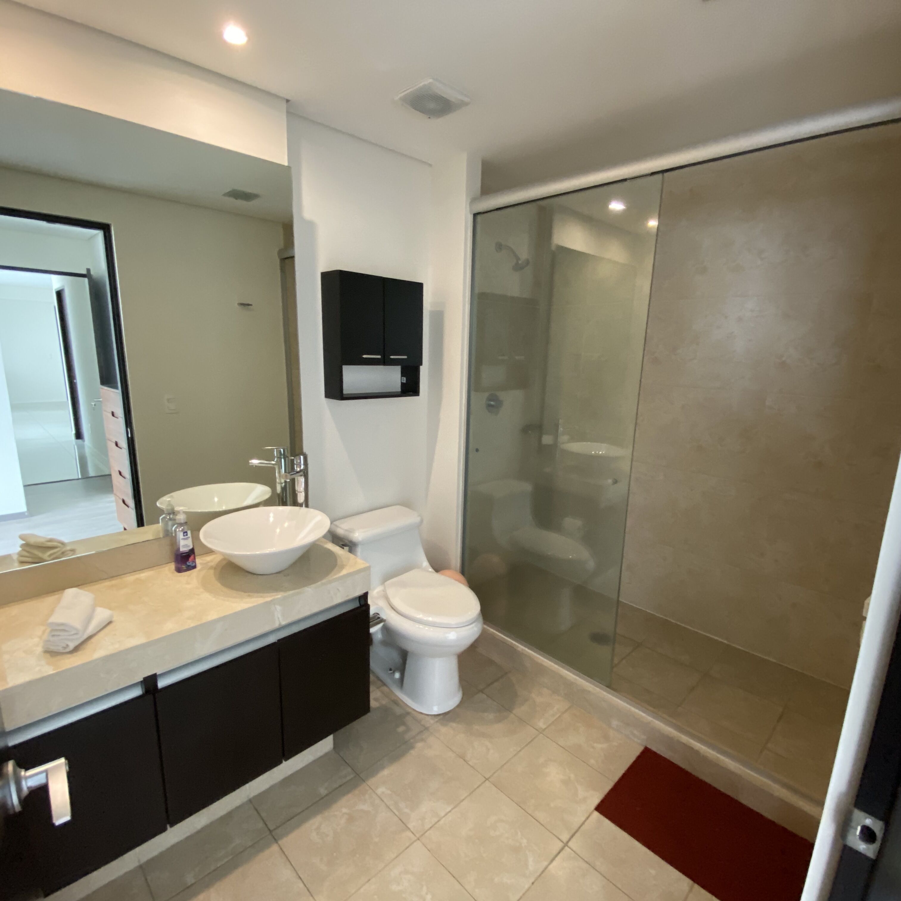 Une salle de bain moderne avec un grand miroir, deux lavabos, des toilettes et une douche à parois de verre.
