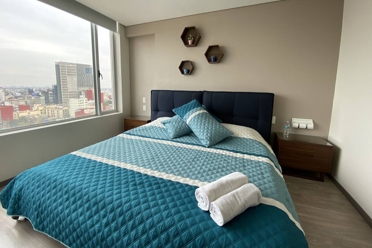 A modern bedroom with a large bed, a city view, and a minimalist decor.