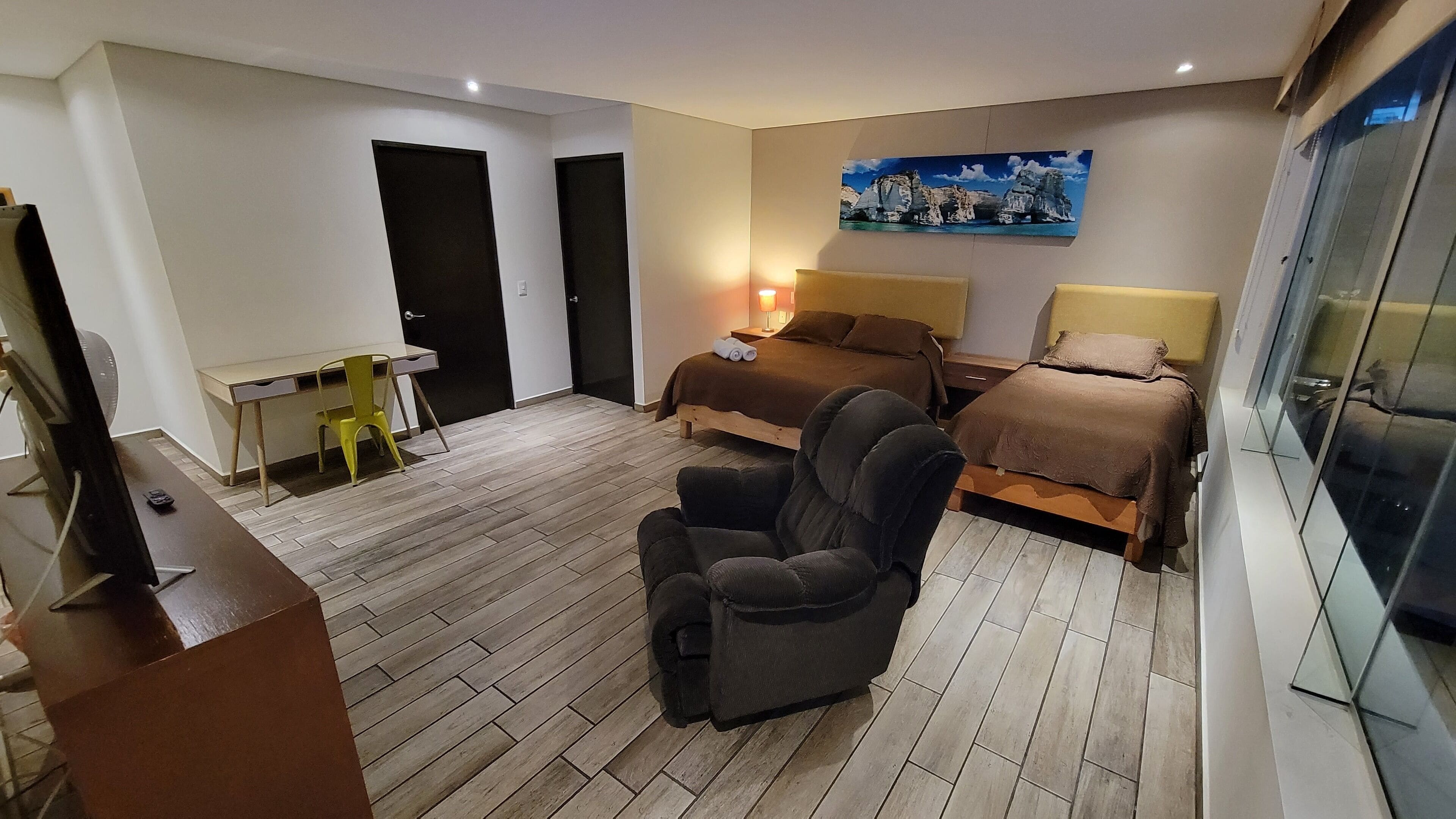 Quarto de hotel com cama, escrivaninha, cadeira e televisão.