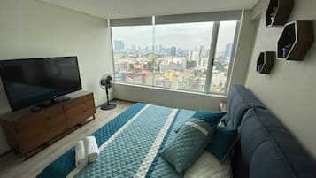 Een slaapkamer met een groot raam, een bed, een televisie, een ventilator en een dressoir.