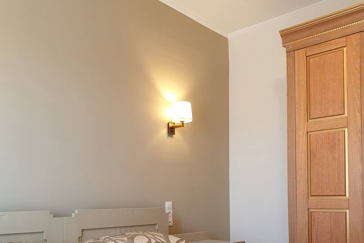 A hotel room with a bed, a wall-mounted lamp, and a wooden wardrobe.